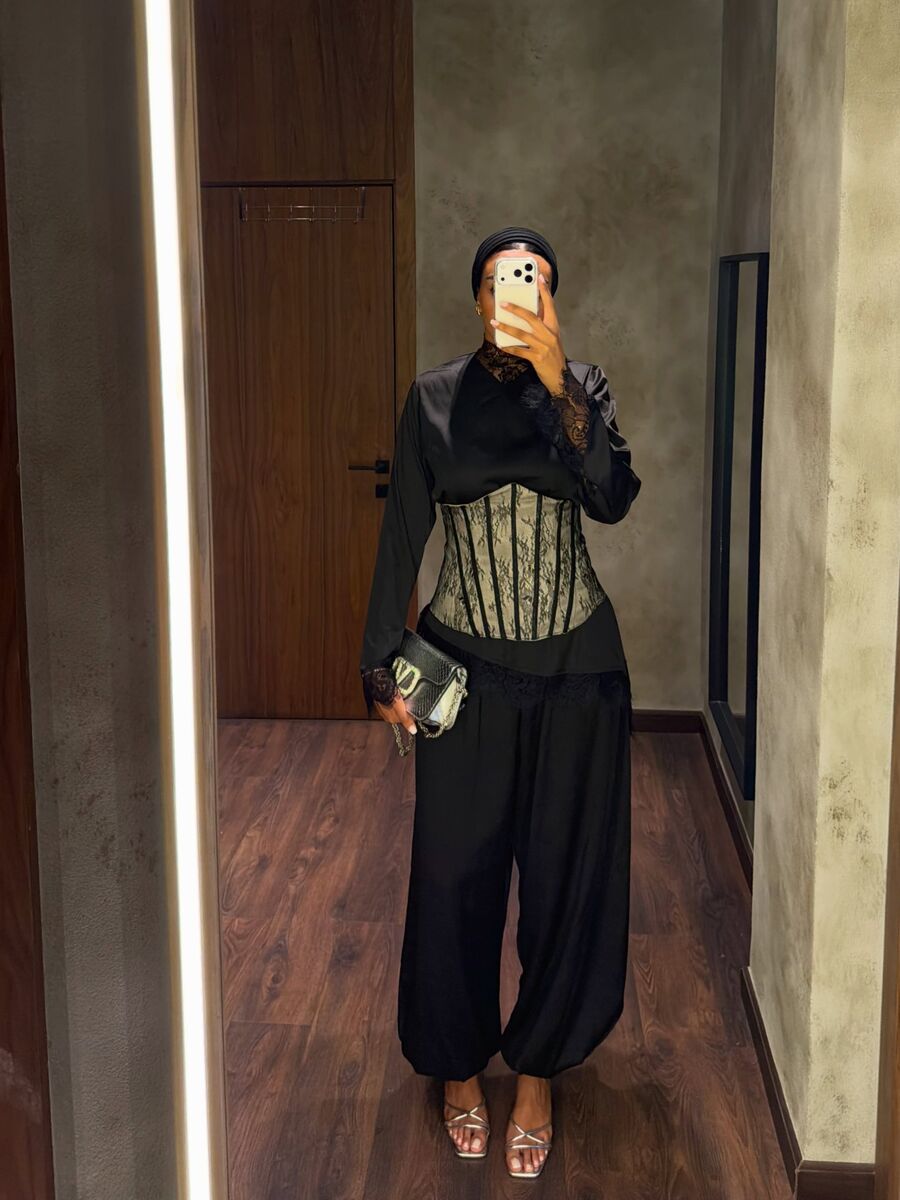 A woman in a black satin top, lace corset and full trousers