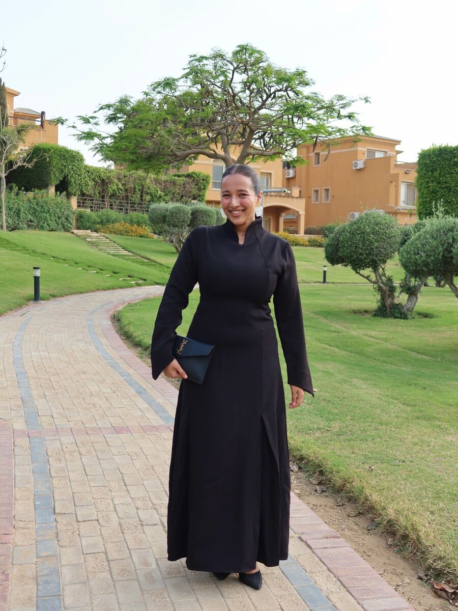 A smiling woman in a long black dress with a high collar, on a garden path