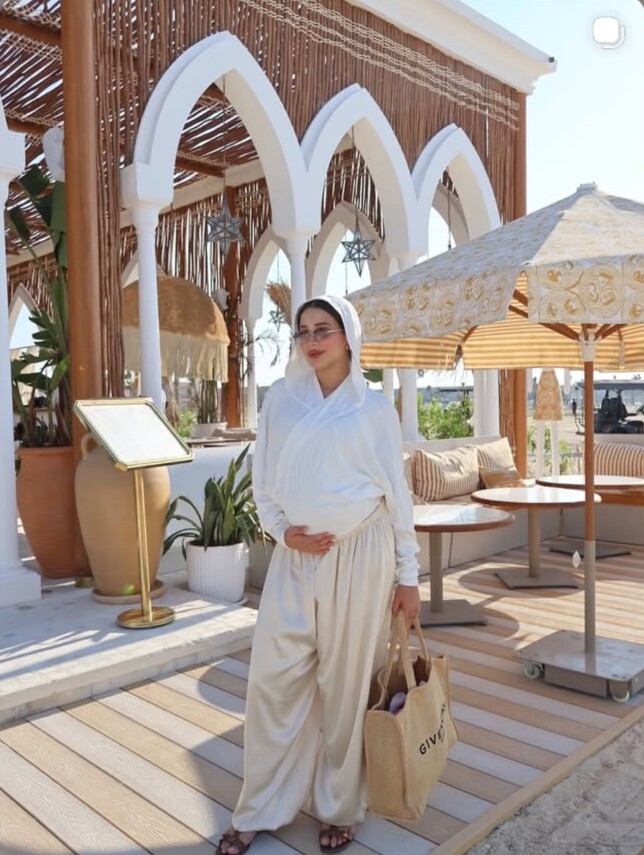 A woman in white with a hood and cream balloon trousers under white arches