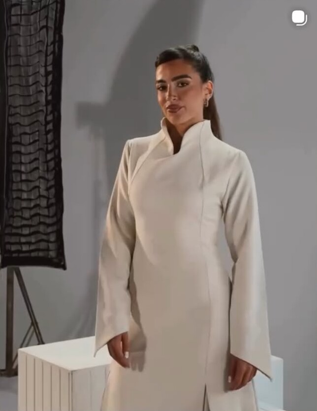 A woman in a cream high-collared maxi dress with long split sleeves