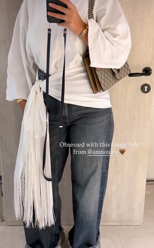 The white fringed wrap tied as a belt over a white shirt and jeans